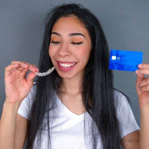 A smiling woman holding an aligner tray in one hand and a credit card in the other.