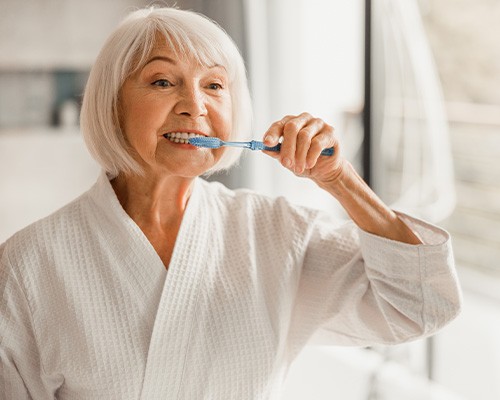 Woman smiling while brushing her teeth in bathroom